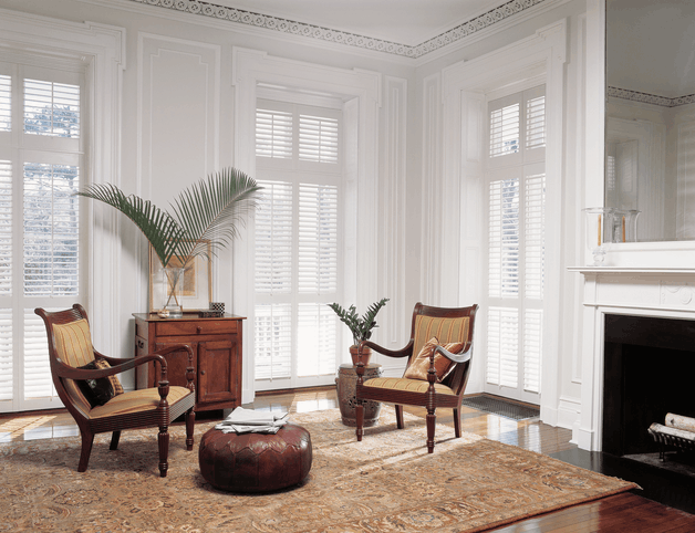 White full height plantation shutters installed in a bright living room, providing full window coverage and a clean, classic look