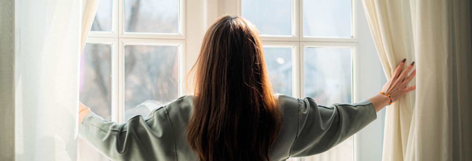 Woman pulling back draperies in winter | Gotcha Covered