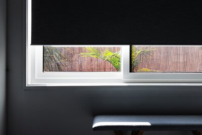 Black blackout roller shade partially raised on a bedroom window