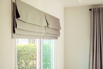 Soft gray Roman shade partially raised alongside a coordinating drapery panel